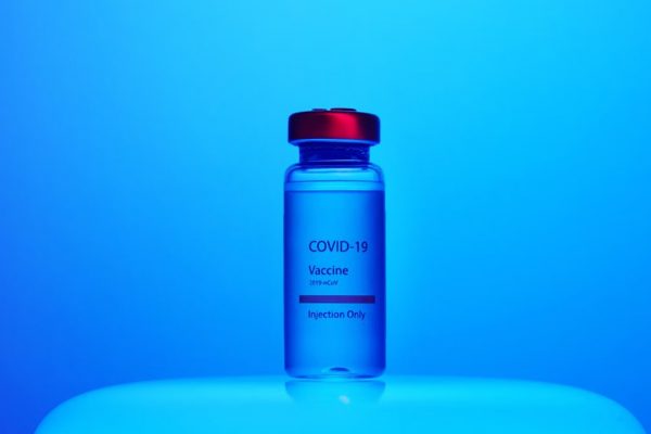Vial of COVID-19 vaccine labeled for injection, set against a blue background.