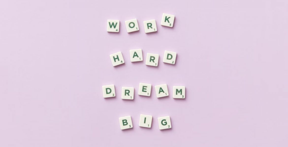 Scrabble tiles spell 'Work Hard Dream Big' on a pastel purple surface, top view.