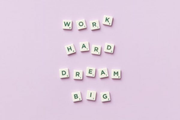 Scrabble tiles spell 'Work Hard Dream Big' on a pastel purple surface, top view.